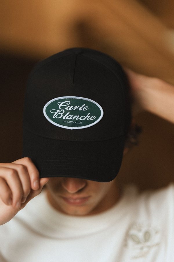 Model tipping a Carte Blanche cap toward the camera, 013 campaign still