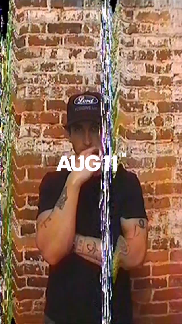 Model in an AUG11 cap against a brick wall, frame from the brand film